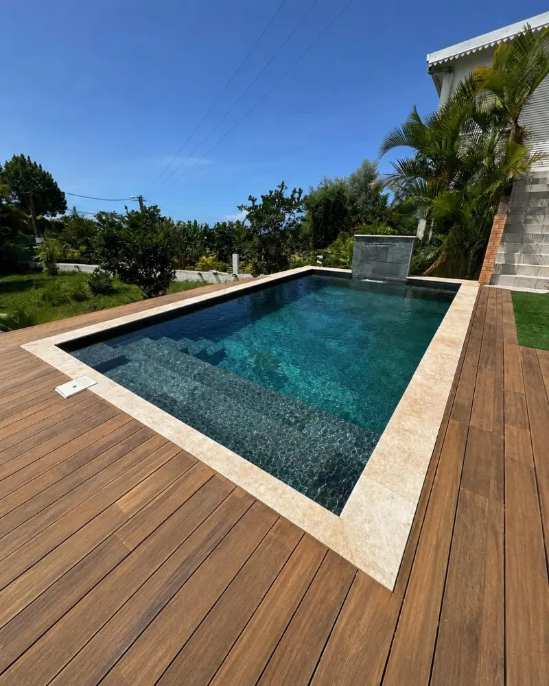 Bassin entouré d'un deck en bois, margelles en pierre claire et lame d'eau